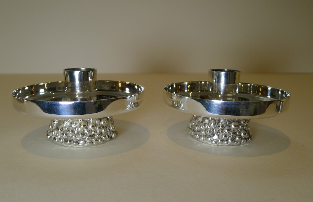 A pair of silver-plated modernist candlesticks featuring wide shallow circular drip trays, cylindrical sockets, and pebbled textured bases. View XI