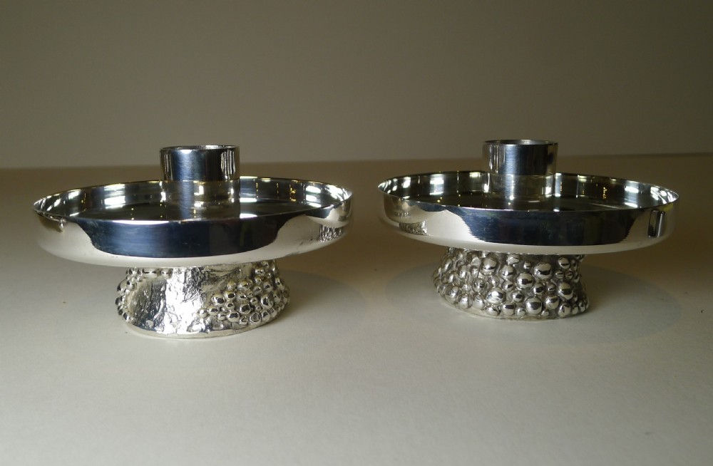A pair of silver-plated modernist candlesticks featuring wide shallow circular drip trays, cylindrical sockets, and pebbled textured bases. View XII
