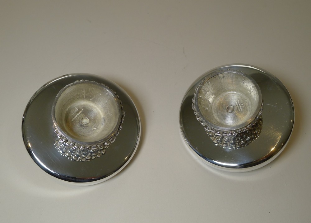 A pair of silver-plated modernist candlesticks featuring wide shallow circular drip trays, cylindrical sockets, and pebbled textured bases. View XIV