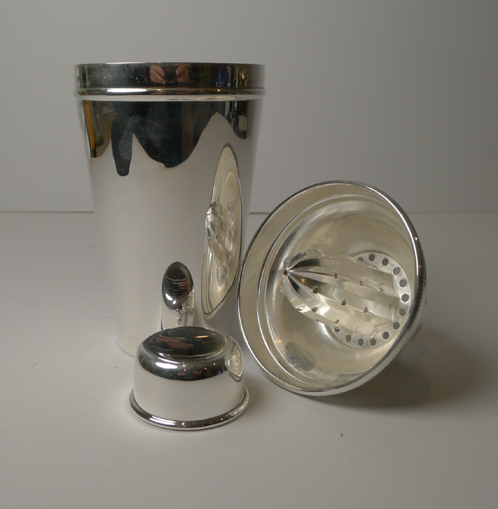 A polished silver-plated cocktail shaker shown disassembled with its cap and integrated lemon squeezer attachment.