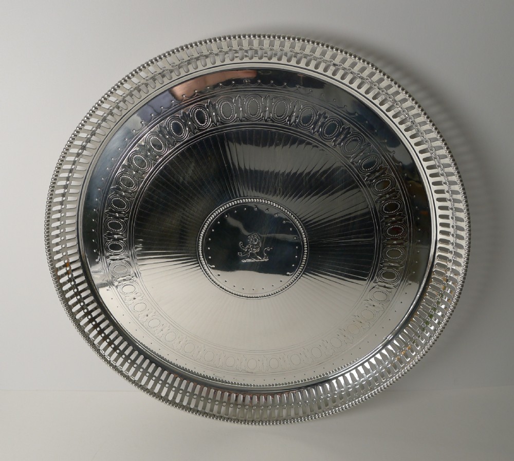 An antique circular silver-plated tray featuring a pierced gallery rim, engine-turned surface patterns, and an engraved heraldic crest in the centre. View III