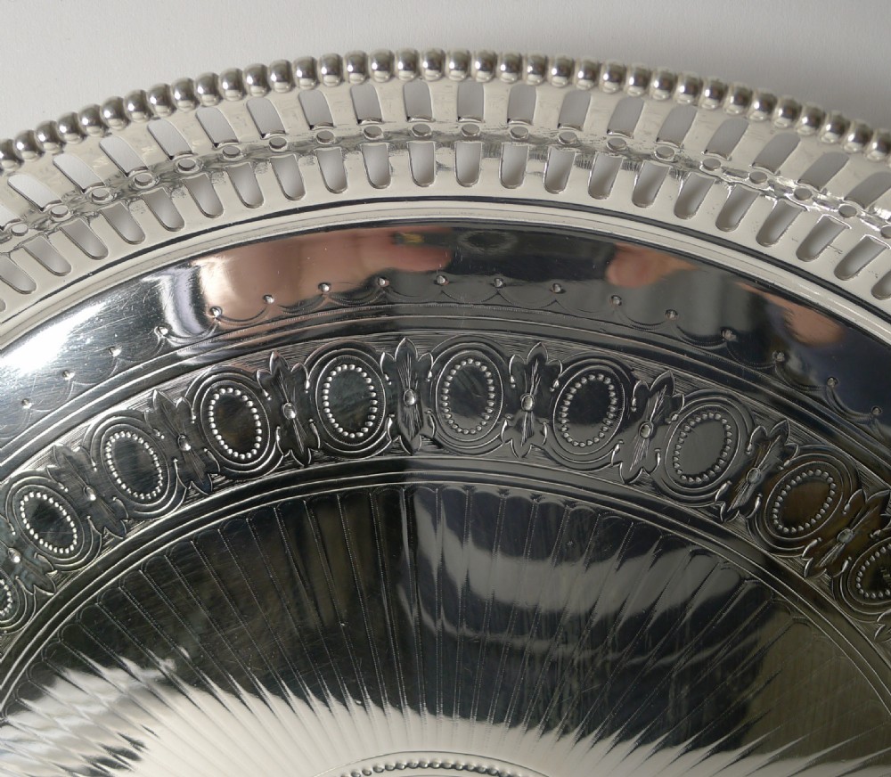 An antique circular silver-plated tray featuring a pierced gallery rim, engine-turned surface patterns, and an engraved heraldic crest in the centre. View IV
