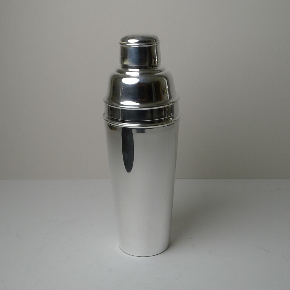 A polished silver-plated Art Deco cocktail shaker featuring a tapered cylindrical body, stepped cap, and smooth reflective finish.