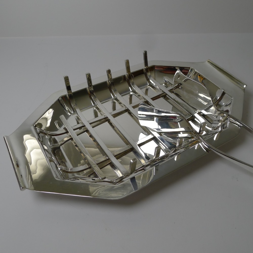 A polished silver-plated octagonal asparagus tray featuring a removable wire draining cradle and matching broad-bladed tongs by Walker and Hall. View V