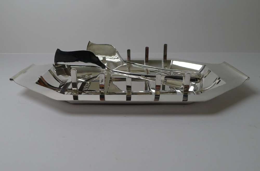 A polished silver-plated octagonal asparagus tray featuring a removable wire draining cradle and matching broad-bladed tongs by Walker and Hall. View VI