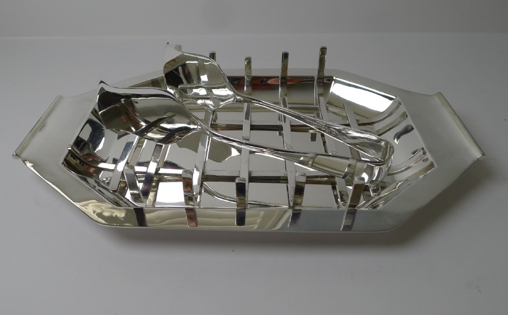 A polished silver-plated octagonal asparagus tray featuring a removable wire draining cradle and matching broad-bladed tongs by Walker and Hall. View VII