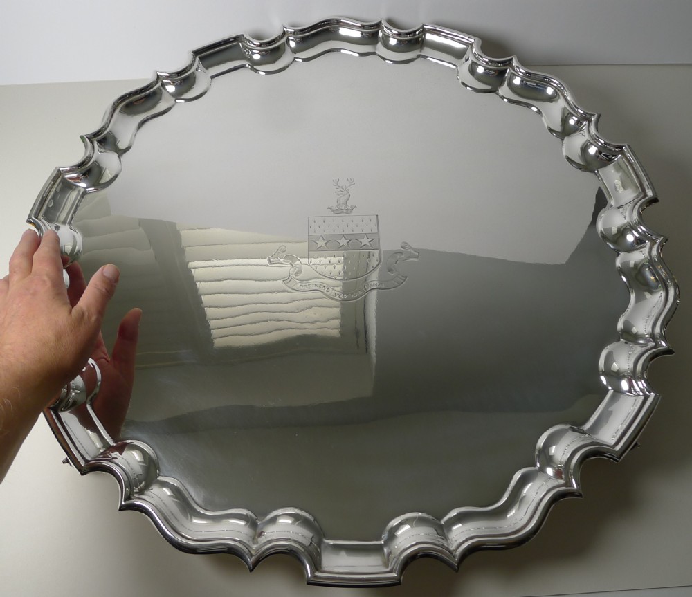 A circular silver-plated salver featuring a scalloped piecrust rim and an engraved armorial family crest in the centre. View II