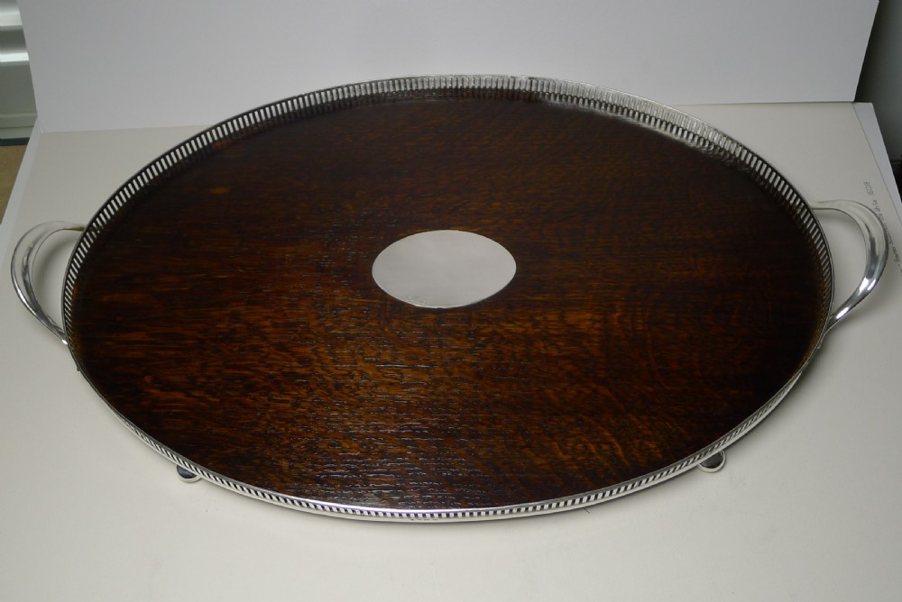 An Edwardian oval dark oak tray featuring a silver pierced gallery border, twin side handles, small bun feet, and a central oval silver medallion.