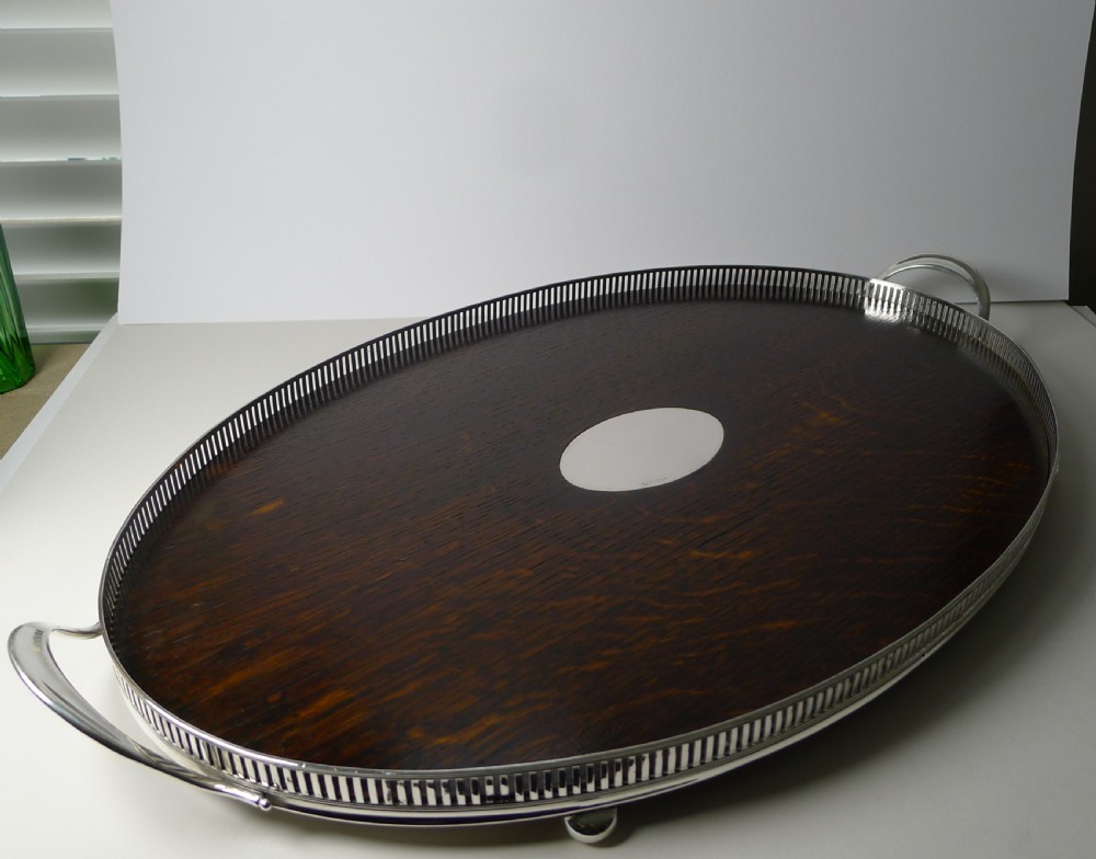 An Edwardian oval dark oak tray featuring a silver pierced gallery border, twin side handles, small bun feet, and a central oval silver medallion. View VII