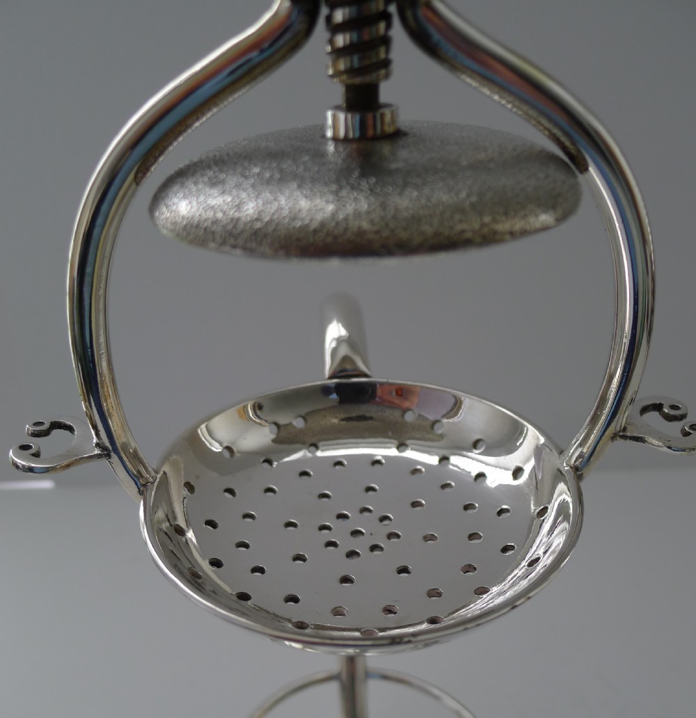 A Victorian silver-plated mechanical lemon squeezer featuring a central screw press mechanism positioned over a perforated strainer and clear glass tumbler. View III
