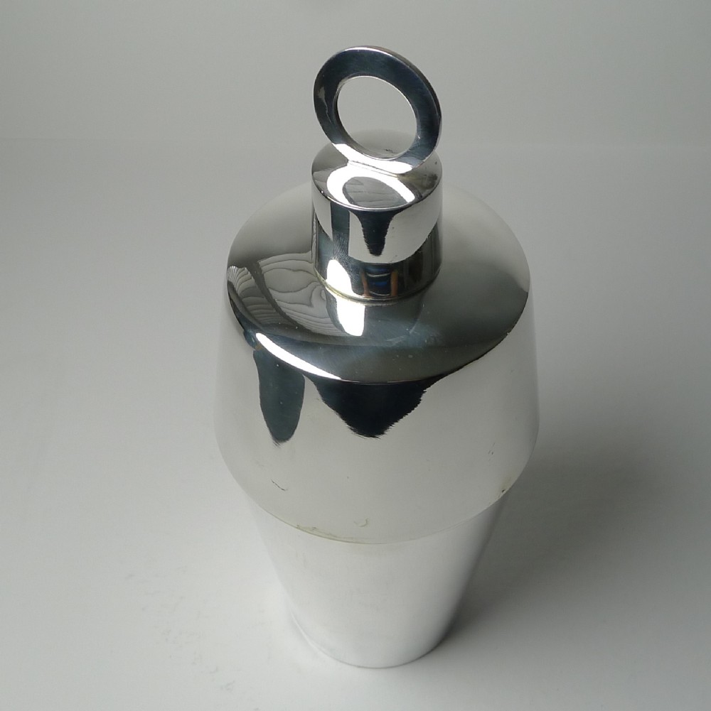 A polished silver-plated Art Deco cocktail shaker featuring a tapered lower body and a cylindrical cap topped with a circular ring finial.