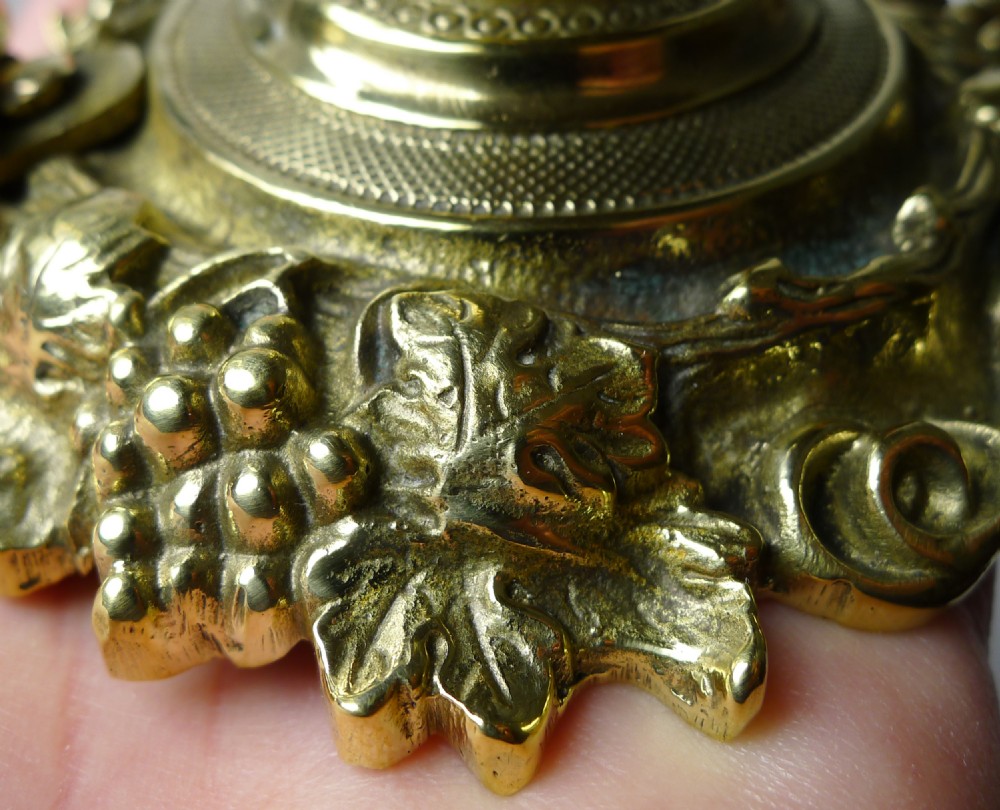 A Victorian polished brass counter desk bell featuring a dome top with a grape motif finial, a cast leafy base, and a side lever mechanism. View IX