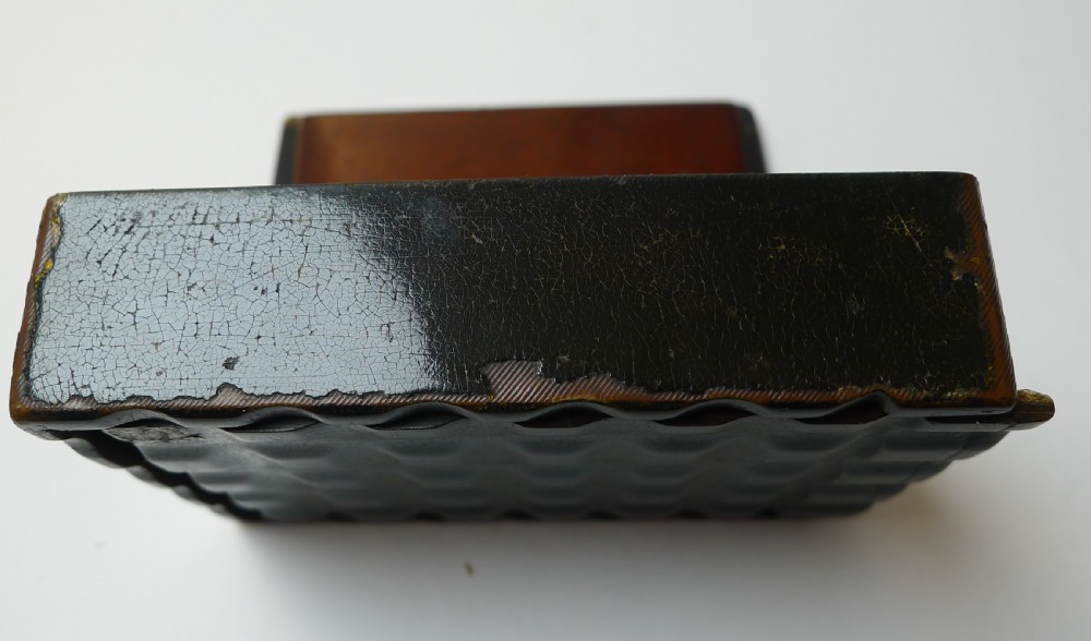 A rectangular black lacquered papier-mache box with a textured waffle-pattern sliding lid revealing a hand-painted classical figurative scene underneath. View V