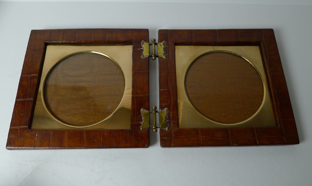 A double folding picture frame bound in brown crocodile-embossed leather featuring circular brass inner apertures and brass hinges. View II