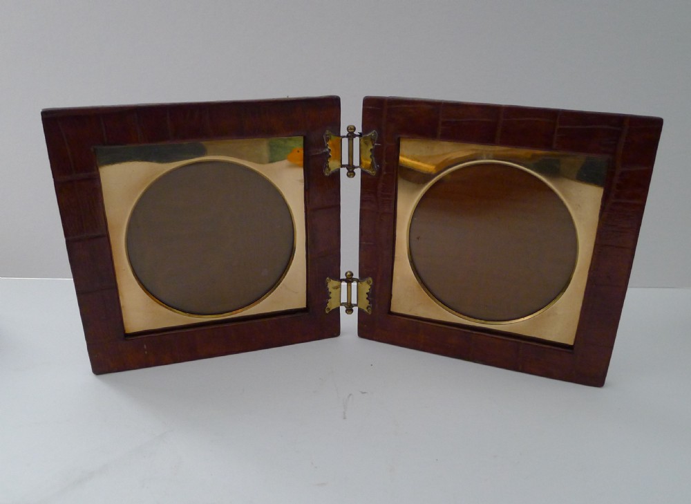 A double folding picture frame bound in brown crocodile-embossed leather featuring circular brass inner apertures and brass hinges. View V