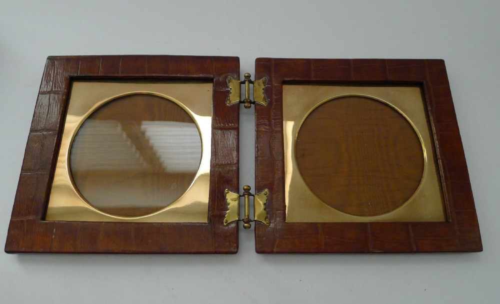 A double folding picture frame bound in brown crocodile-embossed leather featuring circular brass inner apertures and brass hinges. View VIII