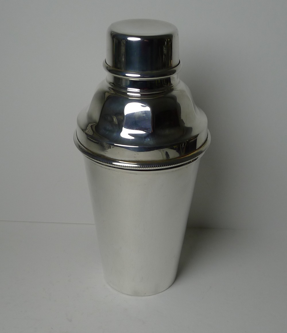 A silver-plated Art Deco cocktail shaker featuring a tapered cylindrical body, fitted cap lid, and smooth polished metallic finish.