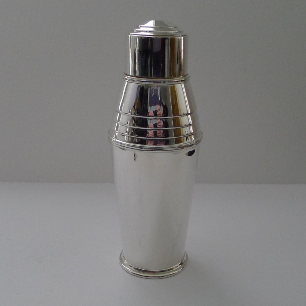A silver-plated Art Deco three-piece cocktail shaker with a stepped cap and concentric banded detailing around the shoulder.