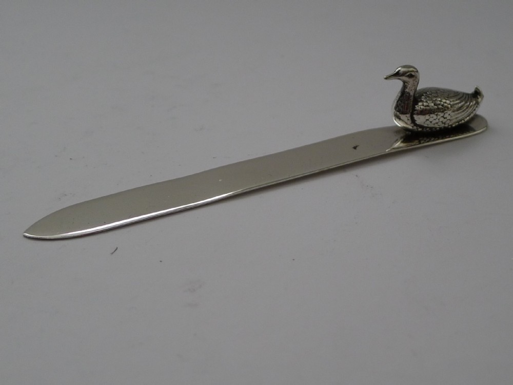 A silver letter opener with a flat polished blade and a cast duck finial positioned at one end.