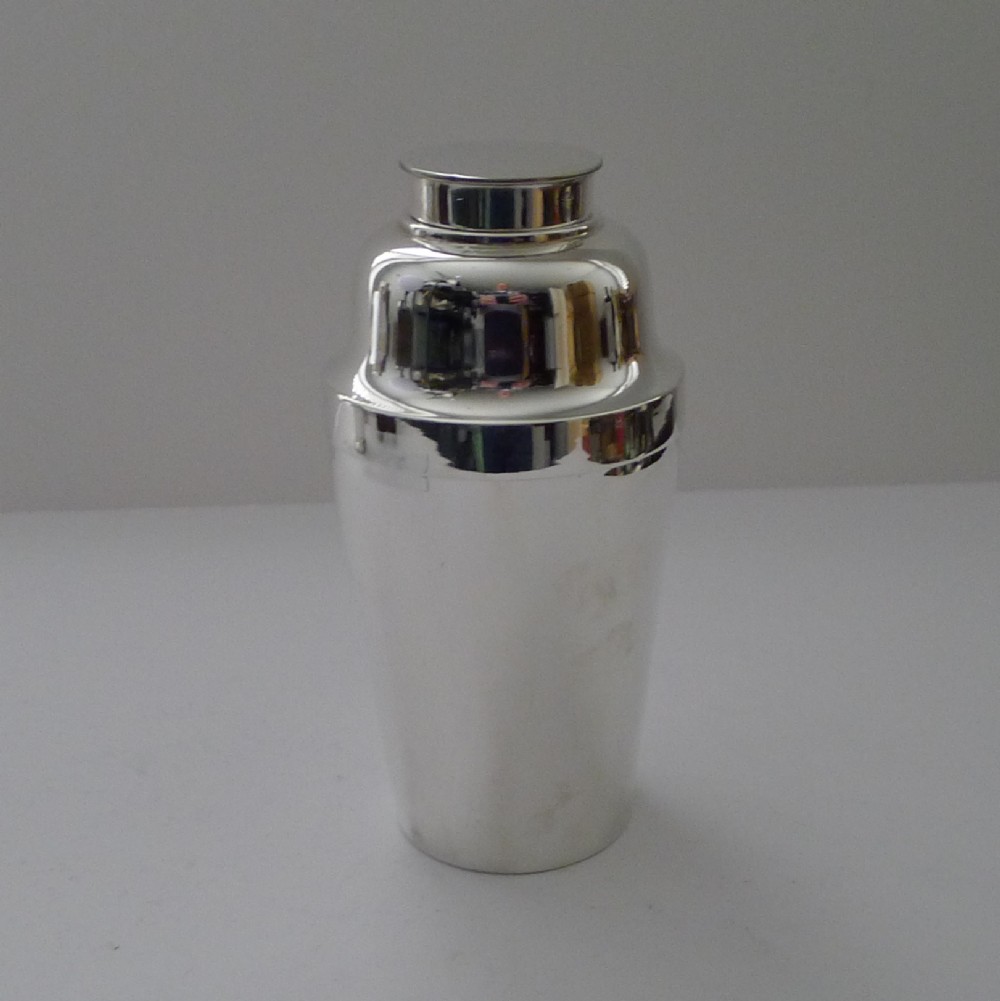 A polished silver-plated Art Deco cocktail shaker with a stepped lid and tapered cylindrical body.