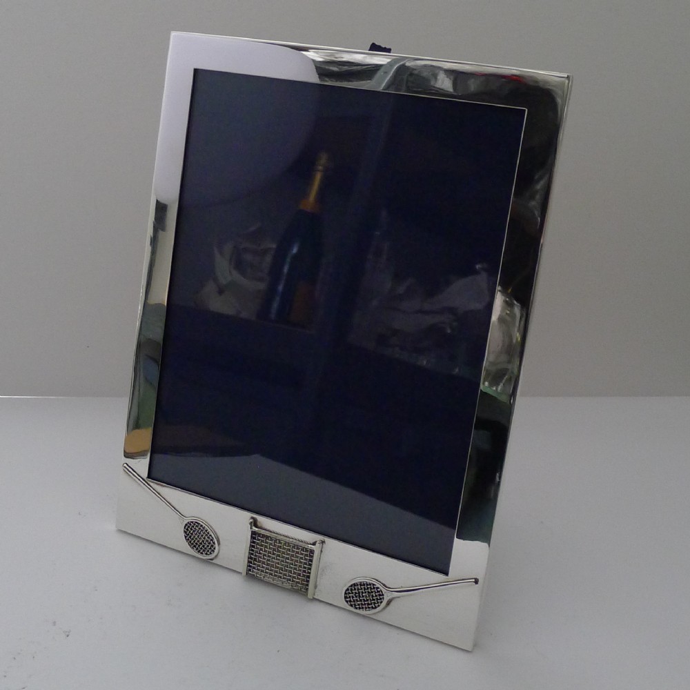 A rectangular sterling silver picture frame featuring miniature relief tennis rackets and a net motif at the bottom edge.