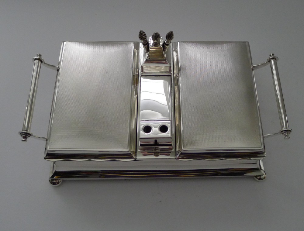 An oblong silver smoking compendium by Mappin & Webb featuring twin hinged lids, central lighter unit with finials, side handles, and a ball-footed base. View III