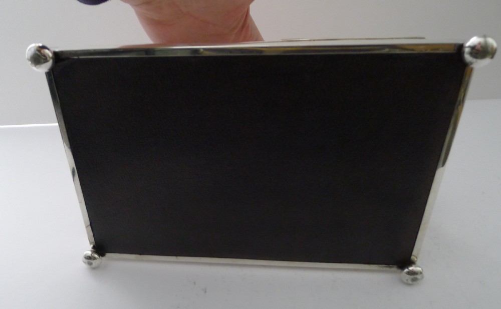 An oblong silver smoking compendium by Mappin & Webb featuring twin hinged lids, central lighter unit with finials, side handles, and a ball-footed base. View VI