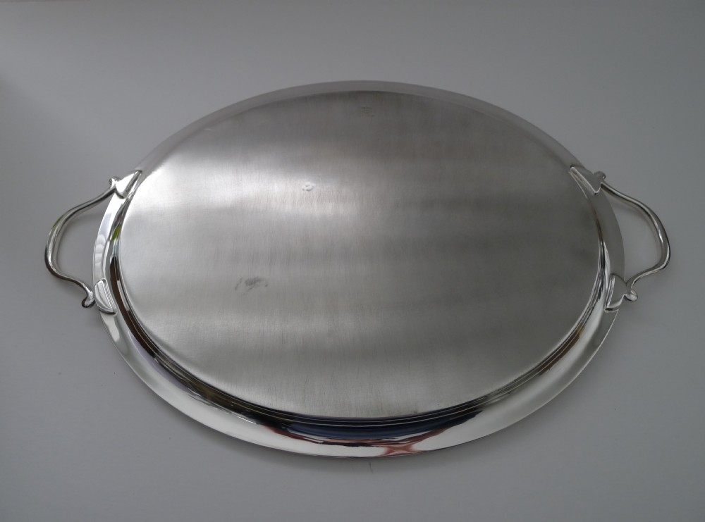 An oval silver-plated Art Deco tray featuring a polished surface, a flat raised rim, and two curved side handles. View V