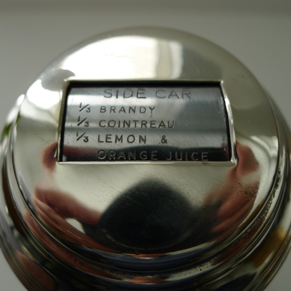 A silver-plated Art Deco cocktail shaker featuring a rotating top cap with rectangular windows displaying drink recipes. View XVII