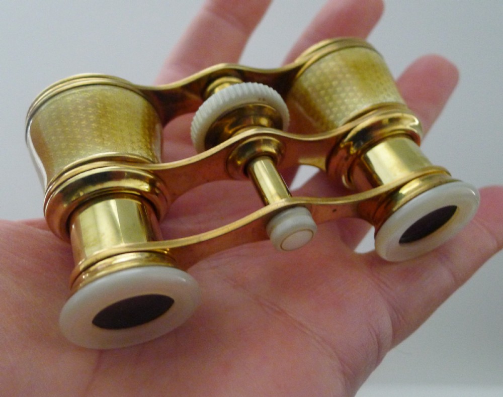 A pair of Edwardian golden guilloche enamel opera glasses with mother-of-pearl eye cups set in front of a grey leather pouch. View V