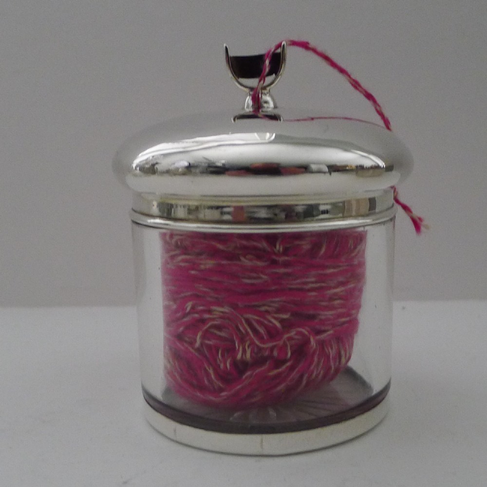 A cylindrical clear glass jar featuring a domed sterling silver lid with a top cutter attachment.