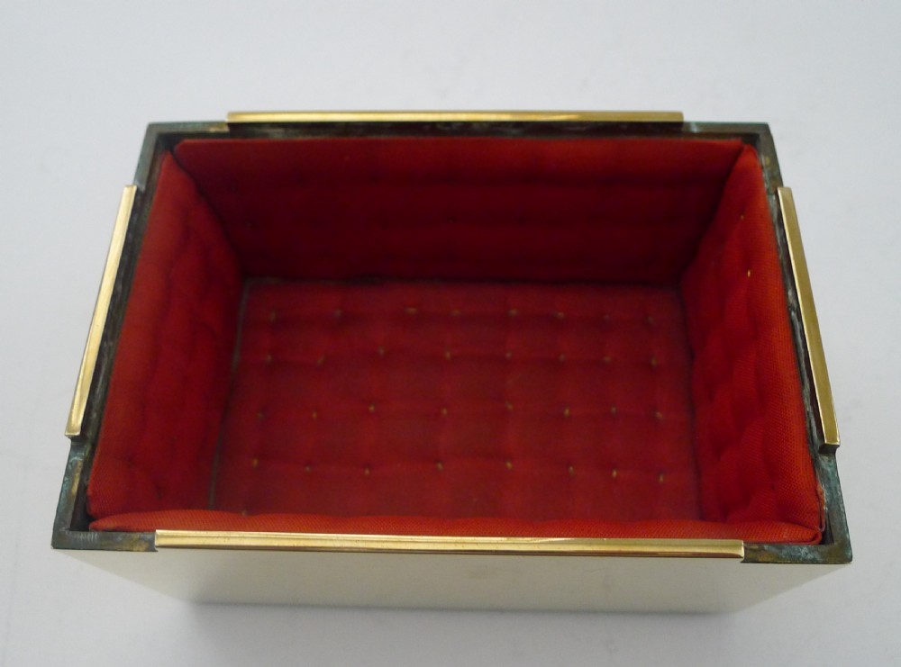 A rectangular polished gold brass casket with an ornate lid motif and red velvet interior. View III