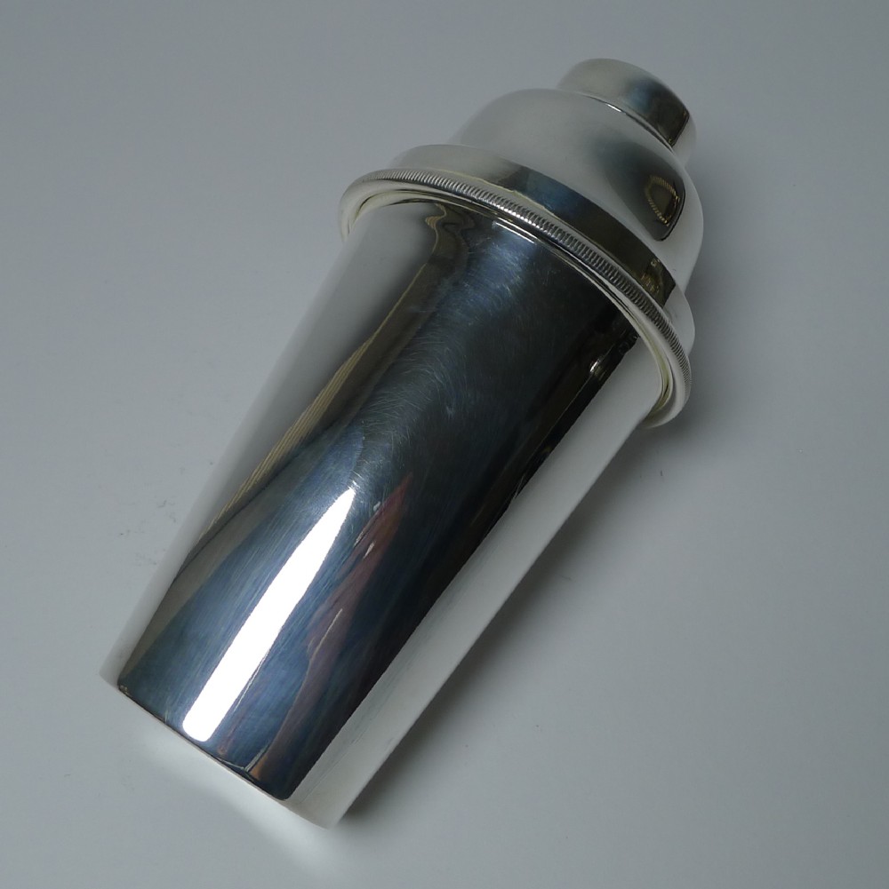 A polished silver-plated Art Deco cocktail shaker featuring a tapered body and a reeded band detail around the upper rim.