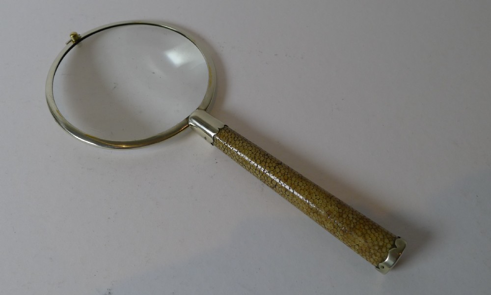 An Art Deco magnifying glass featuring a circular silver-plated rim and a textured brown shagreen cylindrical handle with silver mounts. View VI