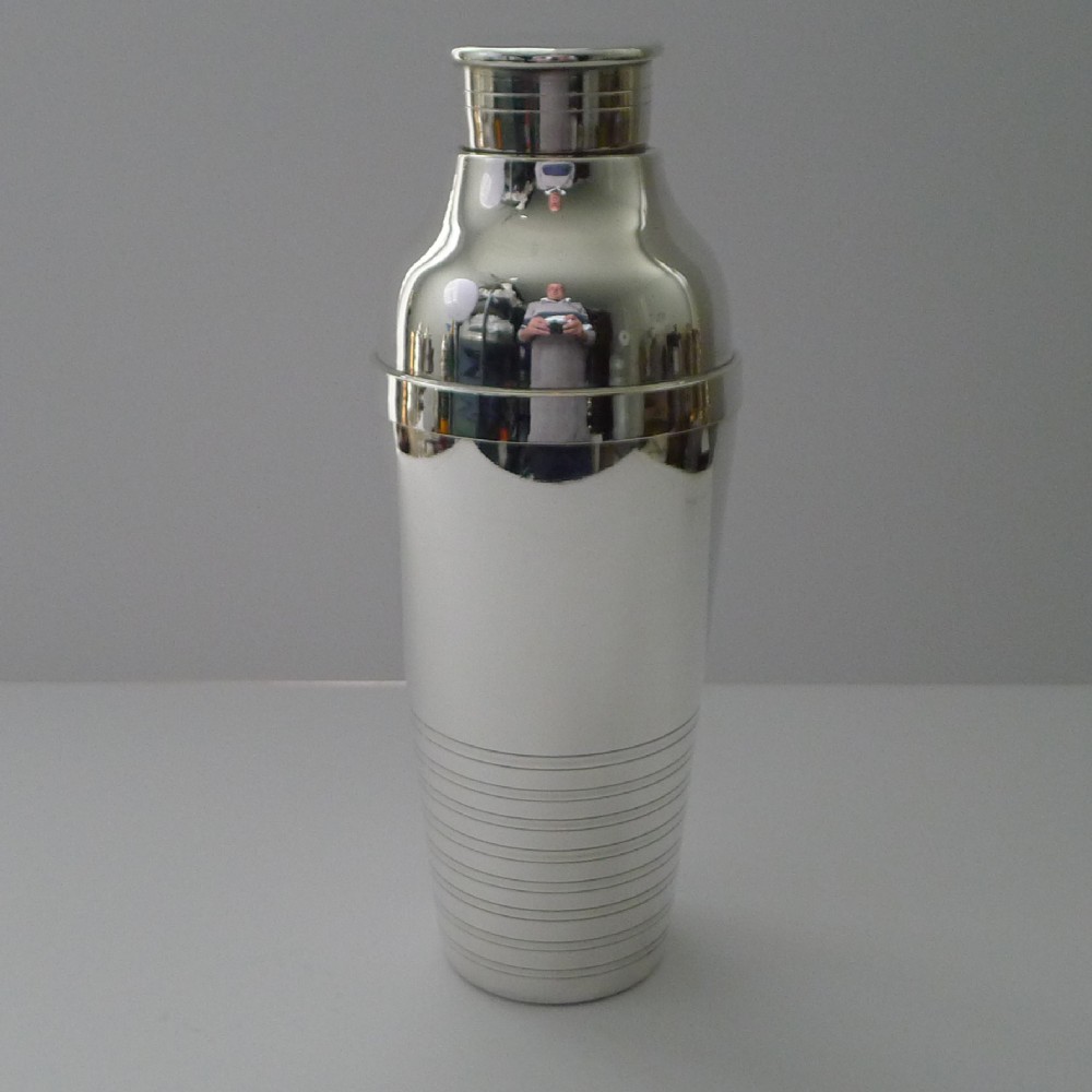A French Art Deco silver-plated cocktail shaker featuring a tapered body with engine-turned horizontal line detailing and a stepped lid.