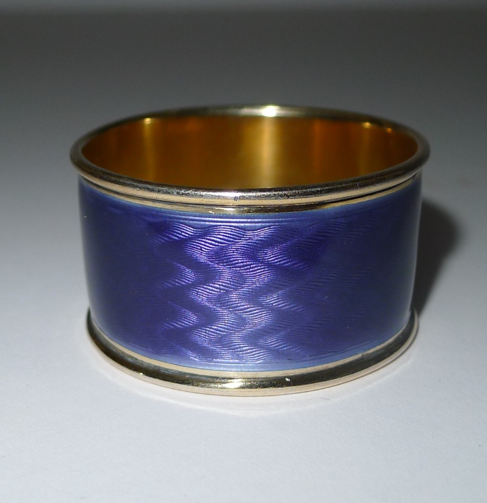 A cylindrical silver-gilt napkin ring featuring a band of vivid cobalt blue guilloche enamel with a wavy engine-turned pattern.