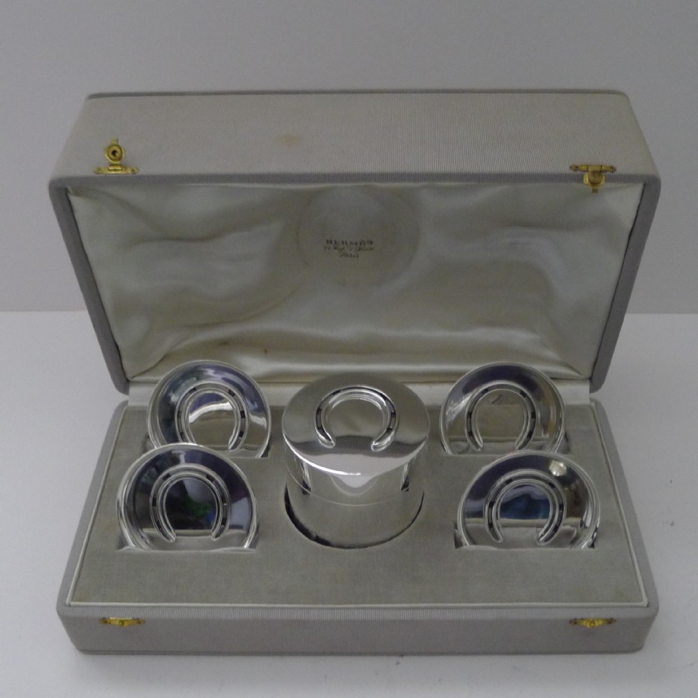 A vintage sterling silver smoking compendium set featuring four horseshoe-shaped ashtrays and a central cylinder within an open silk-lined presentation case.