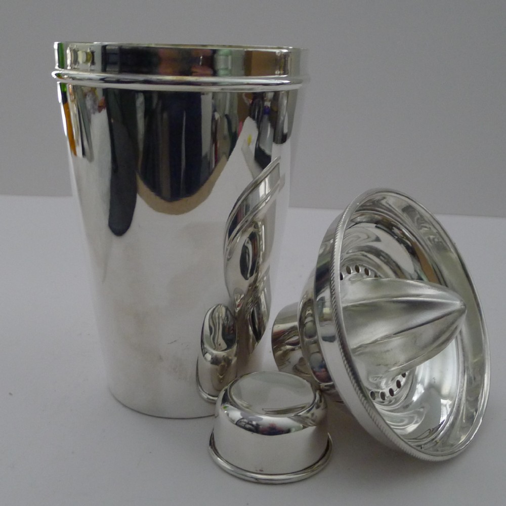 A polished silver-plated cocktail shaker displayed in three sections alongside its integrated citrus reamer lid and cap.