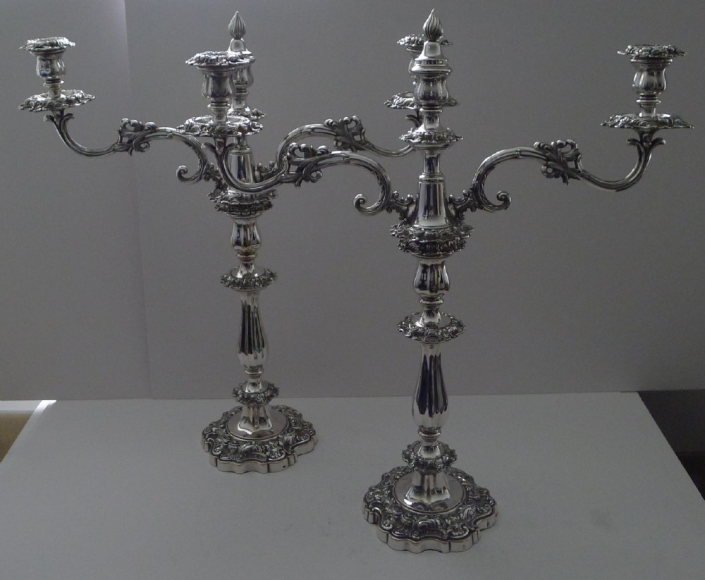 A pair of ornate silver-plated multi-branch candelabra featuring scrolled foliage arms and decorative stepped bases.