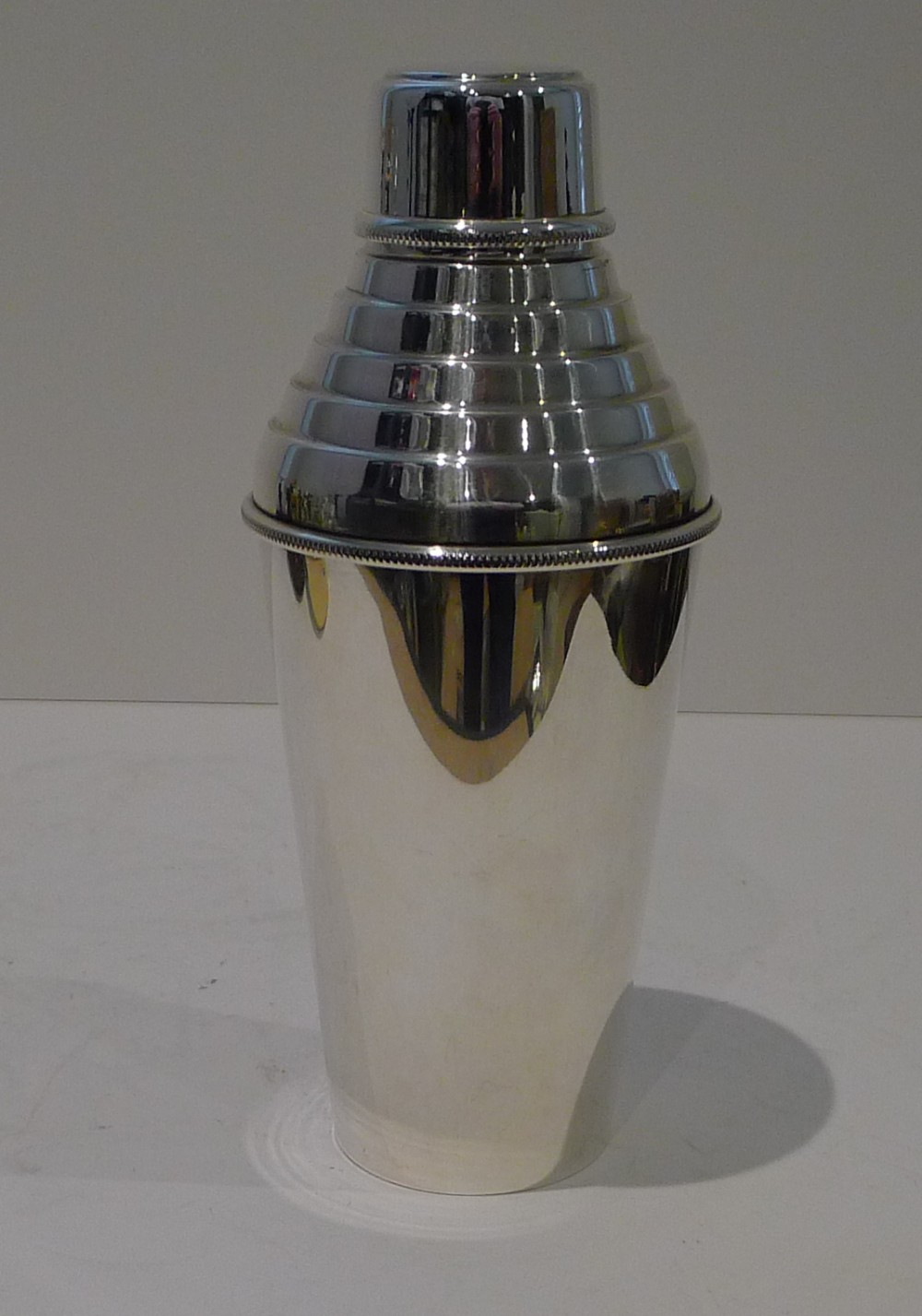 A three-piece Art Deco silver plated cocktail shaker featuring a smooth tapered body with stepped shoulder detailing.