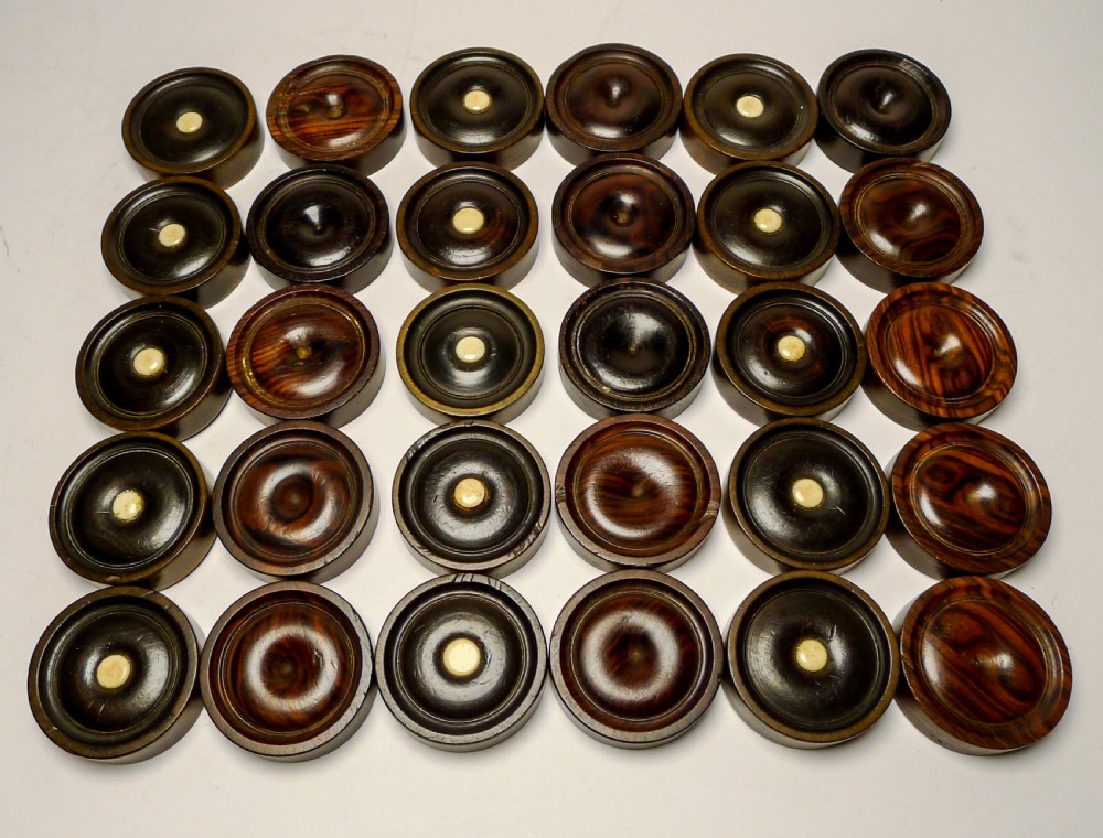 A set of thirty turned dark wooden gaming counters arranged in a grid, featuring central bone inlays and raised circular rims.