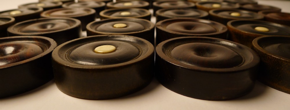 A set of thirty turned dark wooden gaming counters arranged in a grid, featuring central bone inlays and raised circular rims. View III