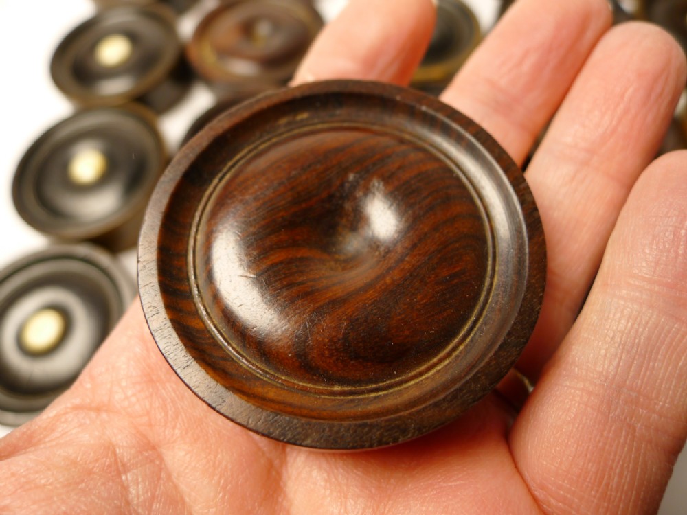 A set of thirty turned dark wooden gaming counters arranged in a grid, featuring central bone inlays and raised circular rims. View V