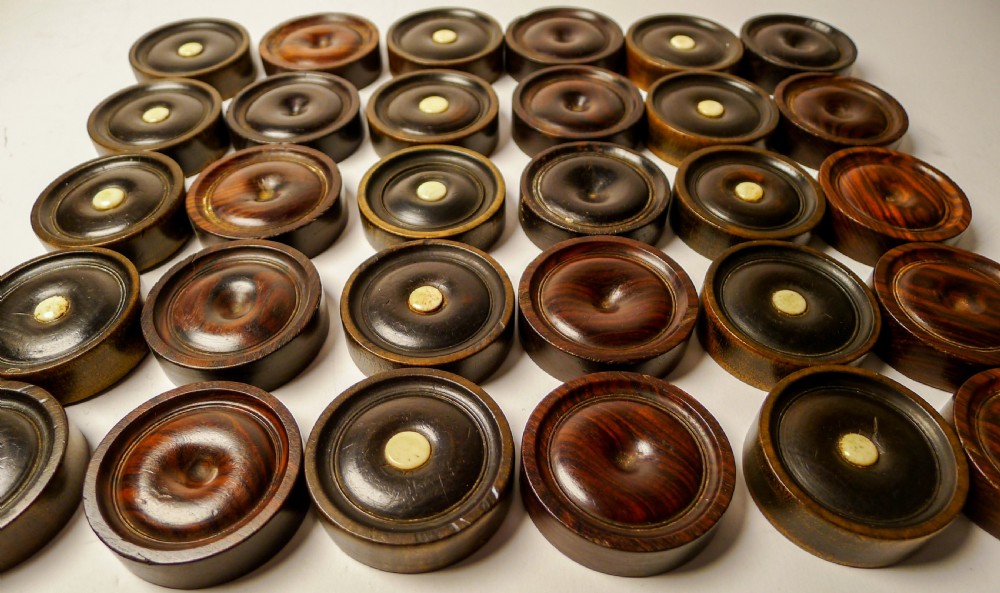 A set of thirty turned dark wooden gaming counters arranged in a grid, featuring central bone inlays and raised circular rims. View VI