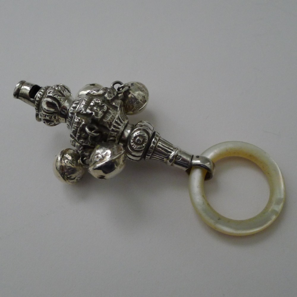 Victorian sterling silver baby rattle featuring intricate embossed detailing, suspended silver bells, an integrated whistle, and a mother-of-pearl teething ring handle.