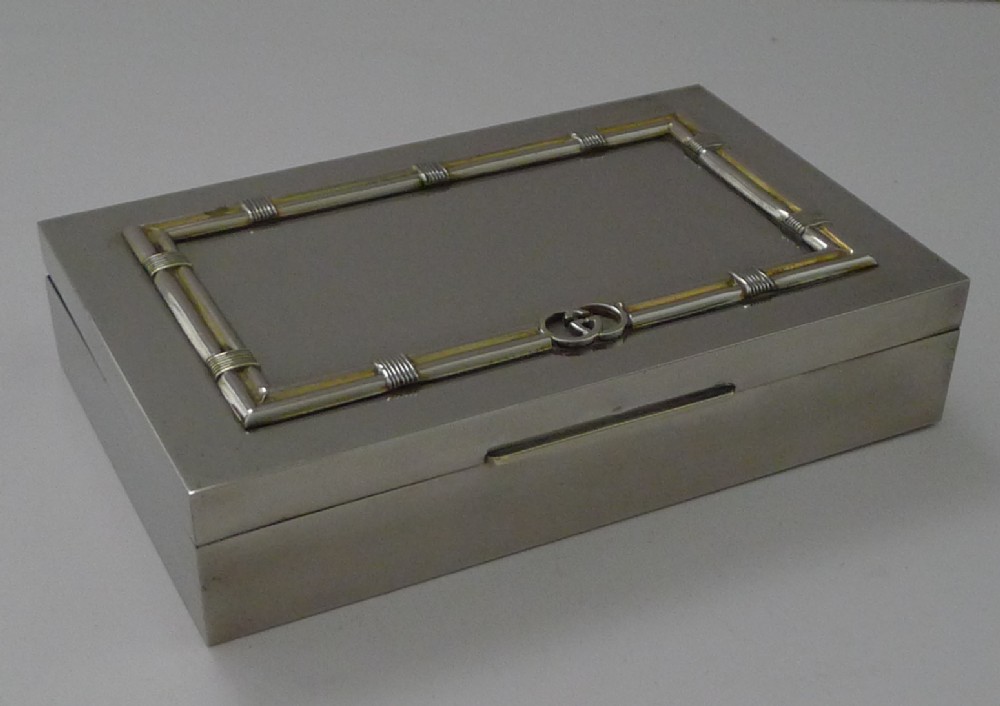 A rectangular silver table box featuring a geometric wire-wrapped border detail and double G emblem on the hinged lid.