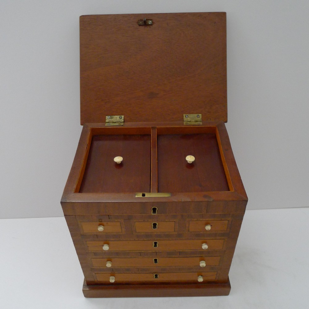 An open Victorian mahogany tea caddy fashioned like a miniature chest of drawers, displaying two inner lidded compartments and decorative inlaid faux drawers. View III