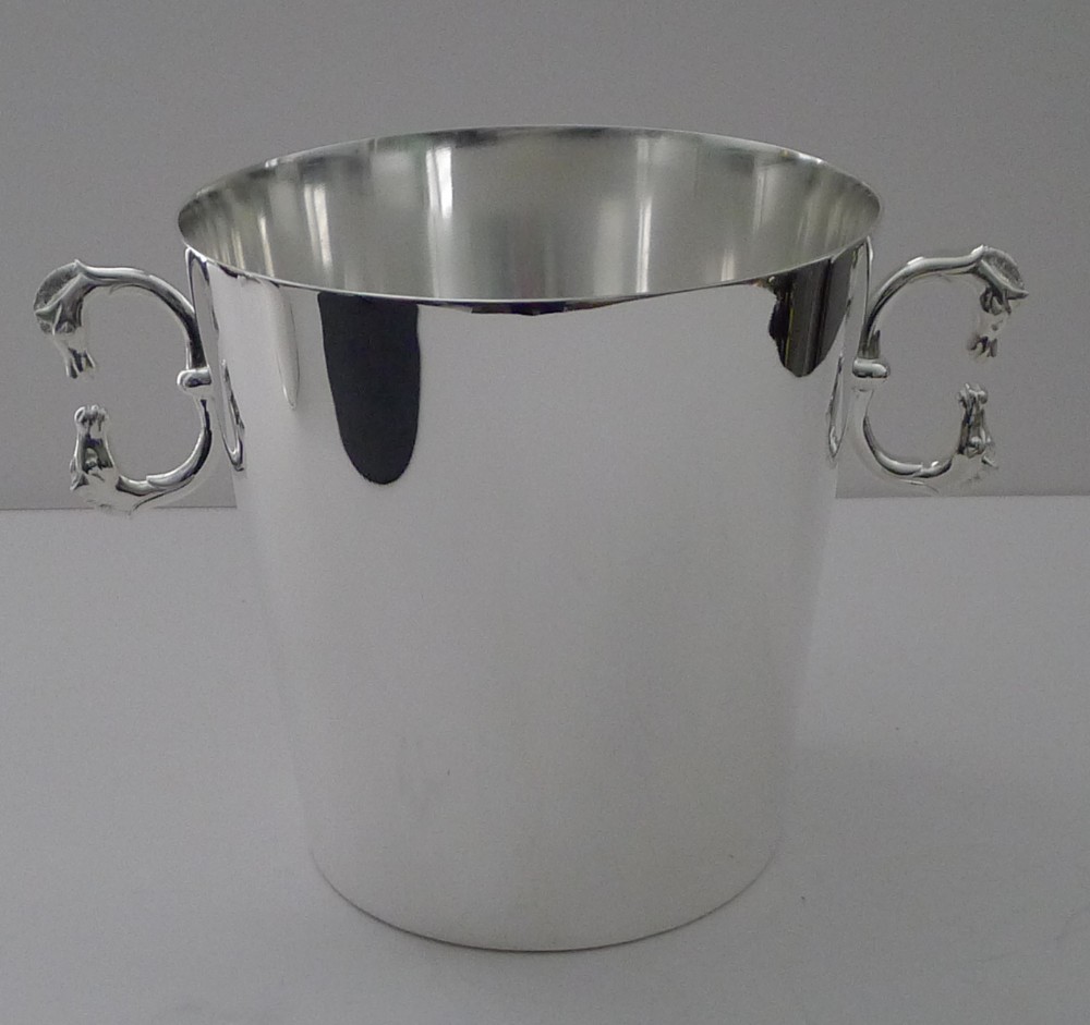 A polished silver-plated champagne bucket featuring twin side handles shaped as detailed horse heads.