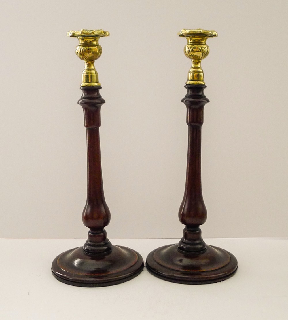 A pair of turned mahogany candlesticks with slender wooden shafts, circular bases, and polished brass sconces.