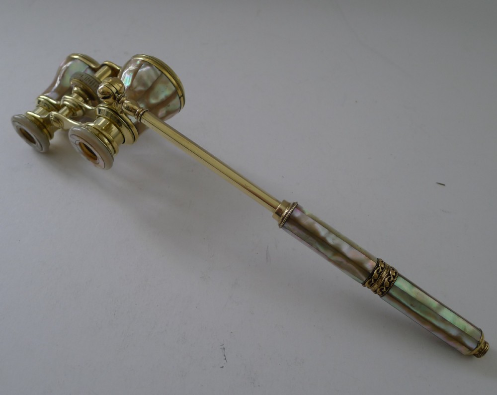 French brass opera glasses featuring mother-of-pearl shell cladding and an extendable side handle on a plain background.